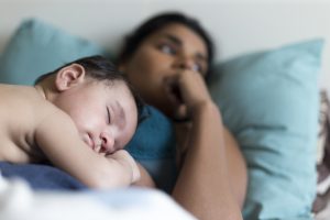 Mother laying on pillow with sleeping baby on her chest